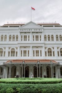 Front facade and entrance of Raffles Hotel Singapore beneath the Singapore flag