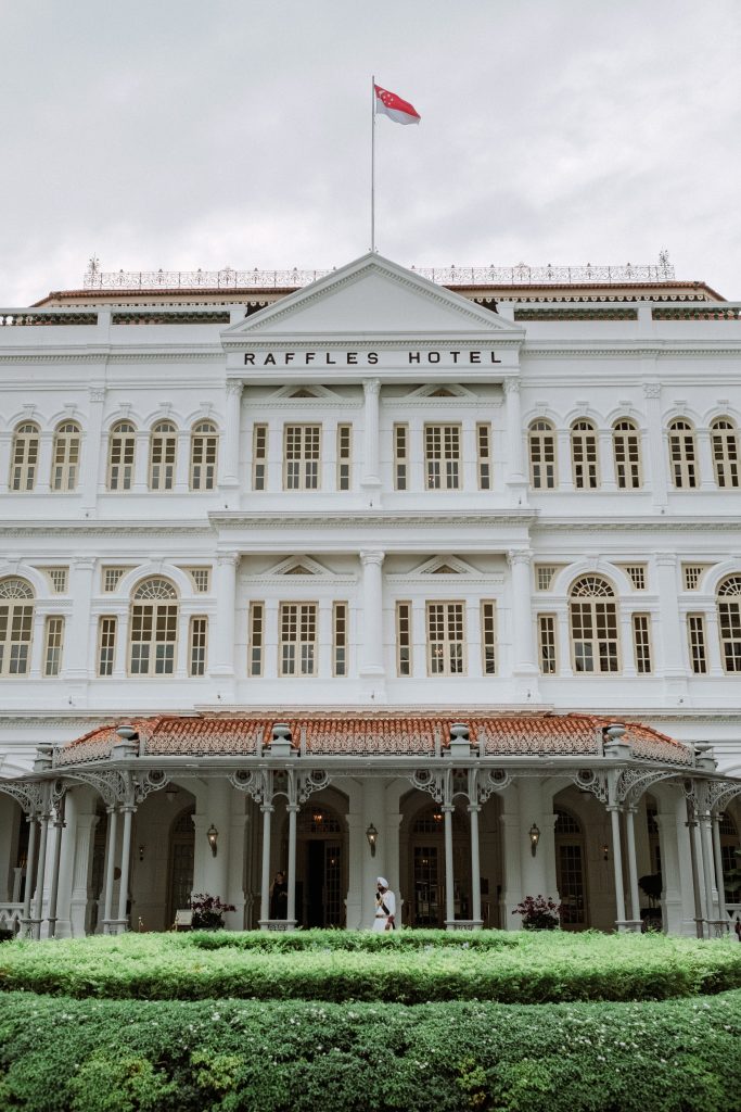 Front facade and entrance of Raffles Hotel Singapore beneath the Singapore flag