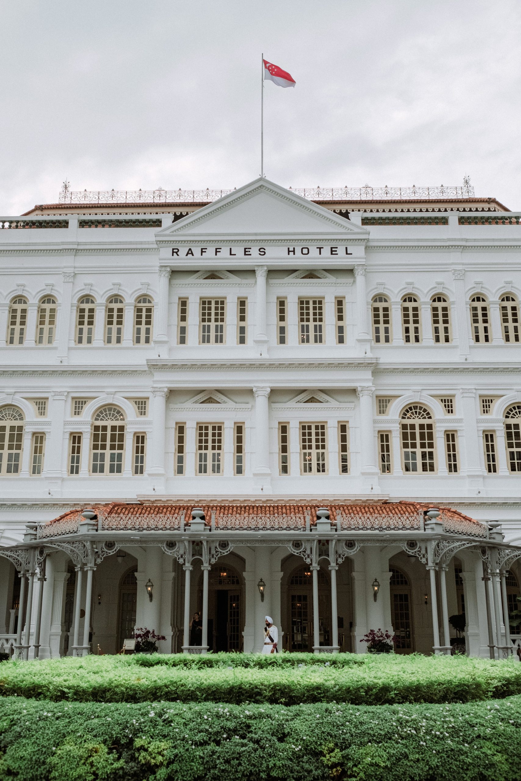 Front facade and entrance of Raffles Hotel Singapore beneath the Singapore flag